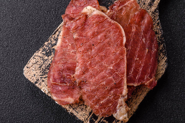 Jerky, dried pork meat slices with salt and spices on a dark concrete background