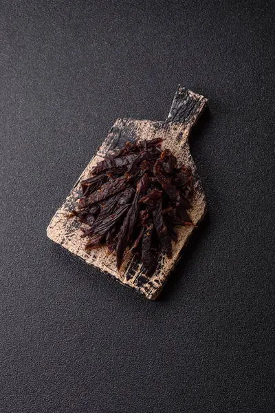 Kurutulmuş at eti ya da koyu beton arka planda tuz ve baharatlı biftek dilimleri.