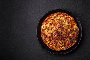 Brokolili, peynirli, baharatlı ve otlu lezzetli taze kiş koyu beton bir arka planda parçalara bölünmüş.