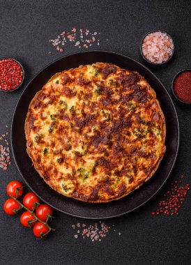 Brokolili, peynirli, baharatlı ve otlu lezzetli taze kiş koyu beton bir arka planda parçalara bölünmüş.