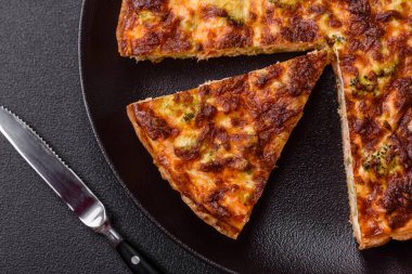 Brokolili, peynirli, baharatlı ve otlu lezzetli taze kiş koyu beton bir arka planda parçalara bölünmüş.