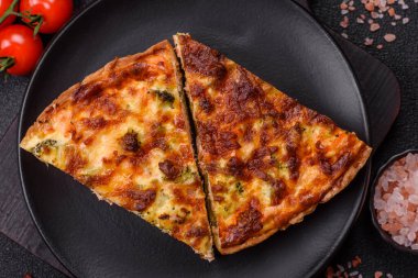 Brokolili, peynirli, baharatlı ve otlu lezzetli taze kiş koyu beton bir arka planda parçalara bölünmüş.