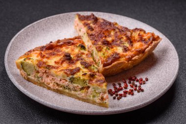 Brokolili, peynirli, baharatlı ve otlu lezzetli taze kiş koyu beton bir arka planda parçalara bölünmüş.