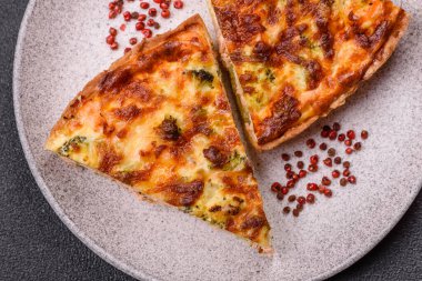 Brokolili, peynirli, baharatlı ve otlu lezzetli taze kiş koyu beton bir arka planda parçalara bölünmüş.