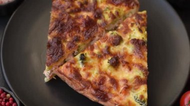 Brokolili, peynirli, baharatlı ve otlu lezzetli taze kiş koyu beton bir arka planda parçalara bölünmüş.