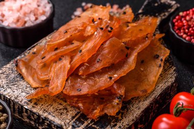 Kurutulmuş, tuzlu ve baharatlı kurutulmuş tavuk eti, koyu beton arka planda.