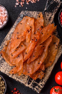 Kurutulmuş, tuzlu ve baharatlı kurutulmuş tavuk eti, koyu beton arka planda.