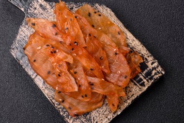 Kurutulmuş, tuzlu ve baharatlı kurutulmuş tavuk eti, koyu beton arka planda.