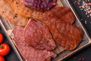 Kurutulmuş et, tuz ve baharatla birlikte koyu beton arka planda.