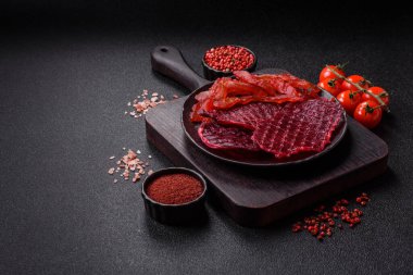 Kurutulmuş sığır eti dilimleri, kurutulmuş et, kiraz veya erik aromalı, tuz ve baharatlar koyu beton arka planda.