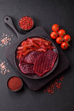 Kurutulmuş sığır eti dilimleri, kurutulmuş et, kiraz veya erik aromalı, tuz ve baharatlar koyu beton arka planda.