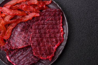 Kurutulmuş sığır eti dilimleri, kurutulmuş et, kiraz veya erik aromalı, tuz ve baharatlar koyu beton arka planda.