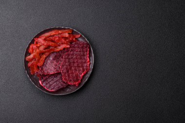 Kurutulmuş sığır eti dilimleri, kurutulmuş et, kiraz veya erik aromalı, tuz ve baharatlar koyu beton arka planda.