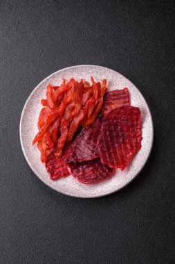 Kurutulmuş sığır eti dilimleri, kurutulmuş et, kiraz veya erik aromalı, tuz ve baharatlar koyu beton arka planda.