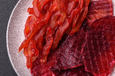 Kurutulmuş sığır eti dilimleri, kurutulmuş et, kiraz veya erik aromalı, tuz ve baharatlar koyu beton arka planda.