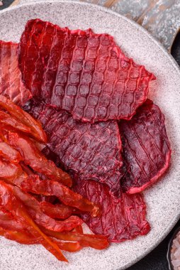 Kurutulmuş sığır eti dilimleri, kurutulmuş et, kiraz veya erik aromalı, tuz ve baharatlar koyu beton arka planda.