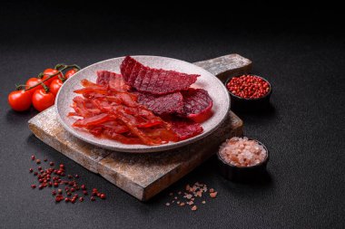 Kurutulmuş sığır eti dilimleri, kurutulmuş et, kiraz veya erik aromalı, tuz ve baharatlar koyu beton arka planda.