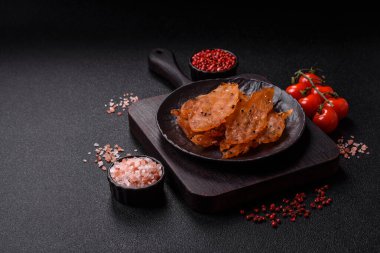 Kurutulmuş, tuzlu ve baharatlı kurutulmuş tavuk eti, koyu beton arka planda.