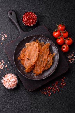 Kurutulmuş, tuzlu ve baharatlı kurutulmuş tavuk eti, koyu beton arka planda.