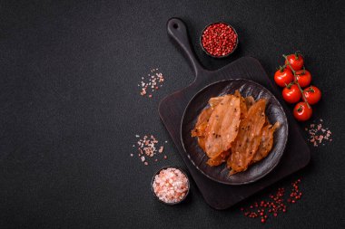 Kurutulmuş, tuzlu ve baharatlı kurutulmuş tavuk eti, koyu beton arka planda.