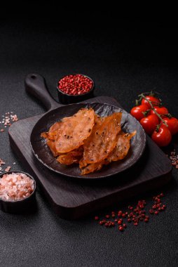 Kurutulmuş, tuzlu ve baharatlı kurutulmuş tavuk eti, koyu beton arka planda.