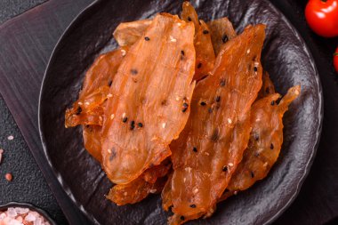 Kurutulmuş, tuzlu ve baharatlı kurutulmuş tavuk eti, koyu beton arka planda.