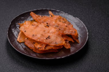 Kurutulmuş, tuzlu ve baharatlı kurutulmuş tavuk eti, koyu beton arka planda.