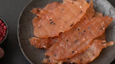 Kurutulmuş, tuzlu ve baharatlı kurutulmuş tavuk eti, koyu beton arka planda.