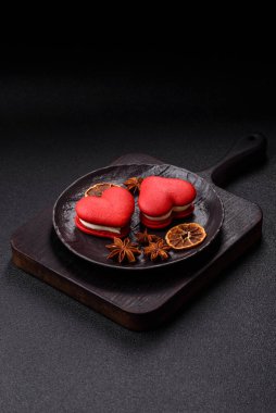 Kalp şeklinde kırmızı badem kurabiyeleri, Sevgililer Günü tatili için tatlılar koyu beton arka planda.