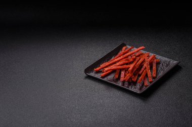 Koyu beton zeminde tuzlu ve baharatlı kurutulmuş balık çubukları.