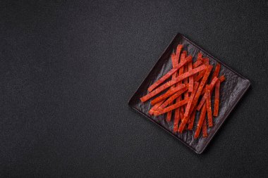 Koyu beton zeminde tuzlu ve baharatlı kurutulmuş balık çubukları.