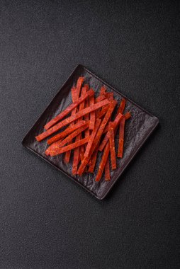 Koyu beton zeminde tuzlu ve baharatlı kurutulmuş balık çubukları.