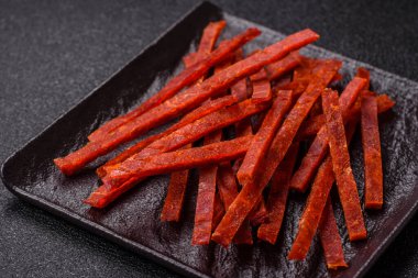 Koyu beton zeminde tuzlu ve baharatlı kurutulmuş balık çubukları.