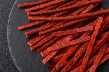 Koyu beton zeminde tuzlu ve baharatlı kurutulmuş balık çubukları.