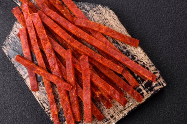 Koyu beton zeminde tuzlu ve baharatlı kurutulmuş balık çubukları.