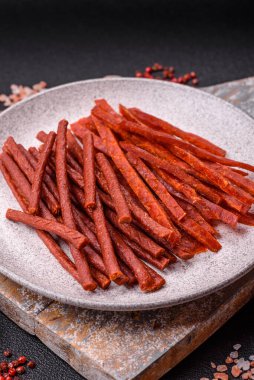 Koyu beton zeminde tuzlu ve baharatlı kurutulmuş balık çubukları.