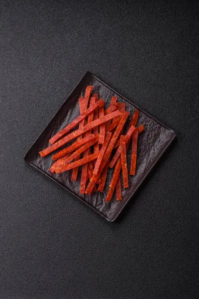 Koyu beton zeminde tuzlu ve baharatlı kurutulmuş balık çubukları.