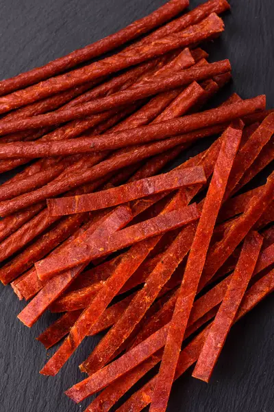 Koyu beton zeminde tuzlu ve baharatlı kurutulmuş balık çubukları.