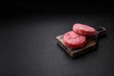 Two fresh slices of raw tuna fillet with spices and herbs on a dark concrete background