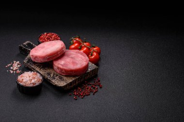 Two fresh slices of raw tuna fillet with spices and herbs on a dark concrete background