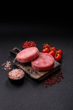 Two fresh slices of raw tuna fillet with spices and herbs on a dark concrete background