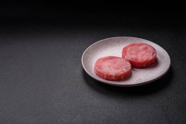 Two fresh slices of raw tuna fillet with spices and herbs on a dark concrete background