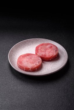 Two fresh slices of raw tuna fillet with spices and herbs on a dark concrete background