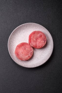 Two fresh slices of raw tuna fillet with spices and herbs on a dark concrete background
