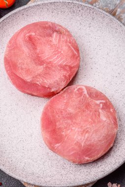 Two fresh slices of raw tuna fillet with spices and herbs on a dark concrete background