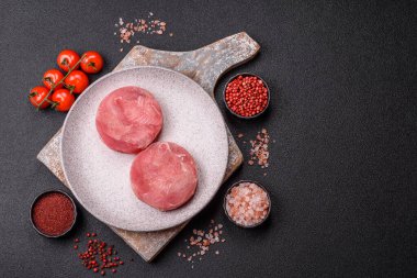 Two fresh slices of raw tuna fillet with spices and herbs on a dark concrete background