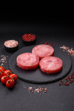 Two fresh slices of raw tuna fillet with spices and herbs on a dark concrete background