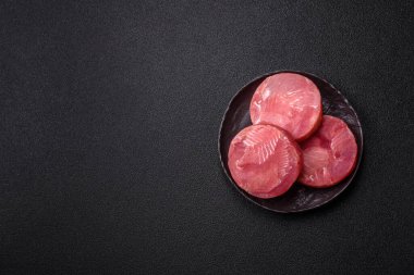 Two fresh slices of raw tuna fillet with spices and herbs on a dark concrete background