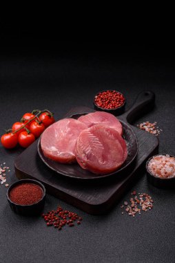 Two fresh slices of raw tuna fillet with spices and herbs on a dark concrete background