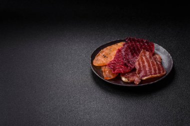 Kurutulmuş et, tuzlu, baharatlı ve otlu dilimler halinde koyu beton bir arka planda.